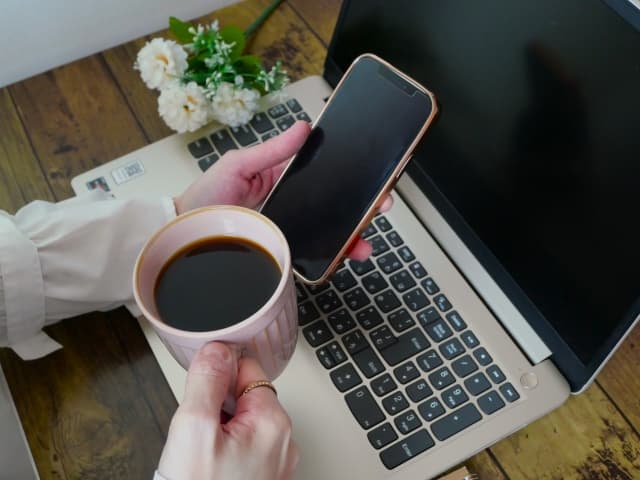 ウェブ制作中 スマホとコーヒーを持つ女性の手